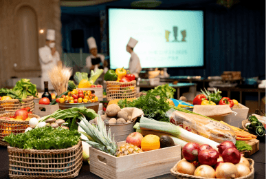 会場内に展示された色鮮やかな新鮮な野菜や果物と、その奥で準備を進めるシェフたち